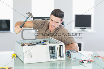 Attractive angry computer engineer destroying computer with hammer