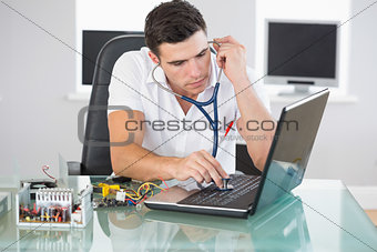 Handsome stern computer engineer examining laptop with stethoscope