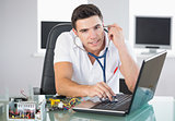 Handsome smiling computer engineer examining laptop with stethoscope