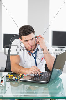 Handsome serious computer engineer examining laptop with stethoscope