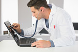 Attractive focused computer engineer examining laptop with stethoscope
