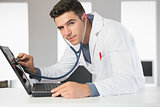 Attractive smiling computer engineer examining laptop with stethoscope