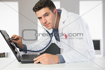 Attractive smiling computer engineer examining laptop with stethoscope