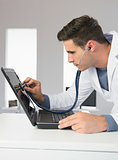 Attractive computer engineer examining laptop with stethoscope