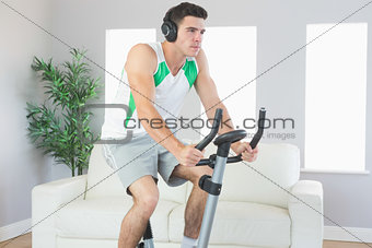 Serious handsome man training on exercise bike listening to music