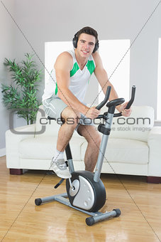 Cheerful handsome man training on exercise bike listening to music