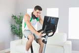 Stern handsome man training on exercise bike using laptop