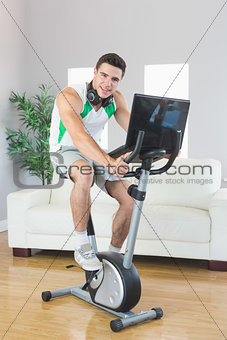 Smiling handsome man training on exercise bike using laptop