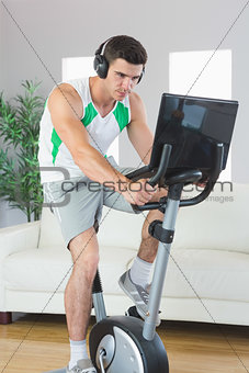 Determined handsome man training on exercise bike using laptop