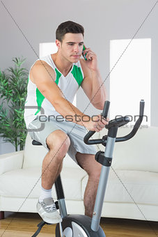 Stern handsome man training on exercise bike phoning