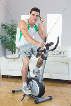 Cheerful handsome man training on exercise bike phoning