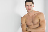 Stern handsome man leaning topless against wall