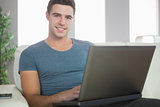 Smiling handsome man relaxing on couch using laptop