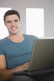 Cheerful handsome man relaxing on couch using laptop