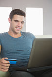 Smiling handsome man relaxing on couch using laptop shopping online