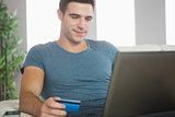Happy handsome man relaxing on couch using laptop shopping online