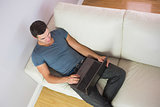 Overhead view of handsome man relaxing on couch using laptop
