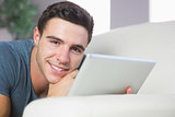 Cheerful handsome man lying on couch using tablet
