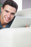 Cheerful atractive man lying on couch using tablet