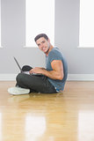 Smiling handsome man using laptop sitting on floor