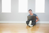Smiling handsome man leaning against wall using laptop