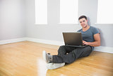 Cheerful handsome man leaning against wall using laptop