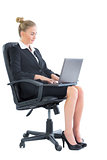 Focused chic businesswoman sitting on an office chair using her laptop
