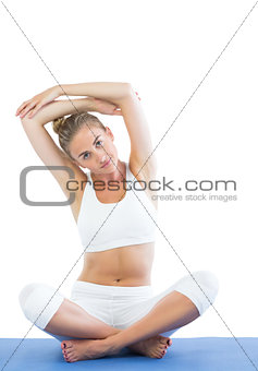 Toned calm blonde sitting on exercise mat stretching arms