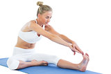 Toned focused blonde sitting on exercise mat stretching right leg