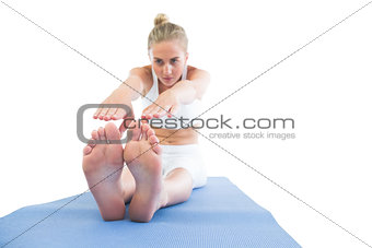 Toned calm blonde sitting on exercise mat stretching legs