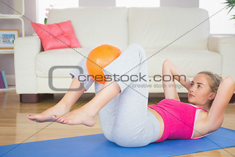 Sporty serious blonde doing sit ups holding ball between knees
