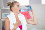 Thirsty blonde sitting on exercise mat drinking from water bottle