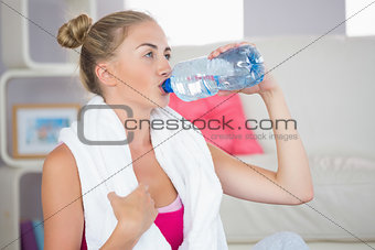 Thirsty blonde sitting on exercise mat drinking from water bottle