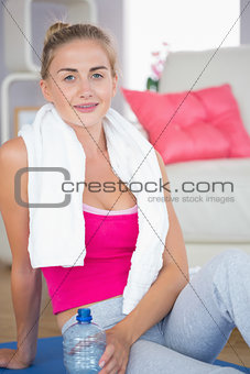 Tired blonde sitting on exercise mat holding water bottle