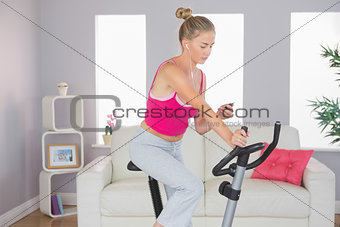 Sporty focused blonde training on exercise bike listening to music