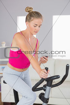 Sporty serious blonde training on exercise bike listening to music