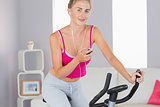 Sporty happy blonde training on exercise bike listening to music