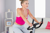 Sporty determined blonde training on exercise bike listening to music