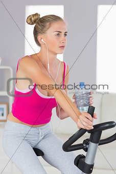 Sporty stern blonde training on exercise bike listening to music
