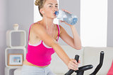 Sporty blonde training on exercise bike drinking water