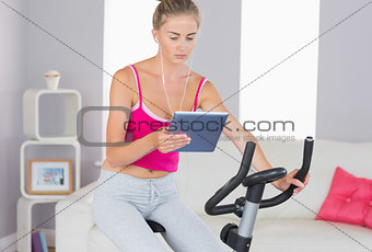 Sporty focused blonde training on exercise bike using tablet