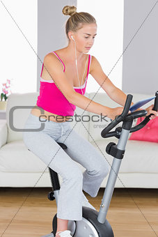 Sporty unsmiling blonde training on exercise bike using tablet