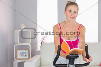 Sporty cheerful blonde training on exercise bike reading a book