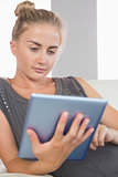 Casual serious blonde relaxing on couch using tablet