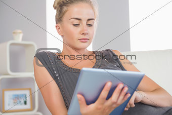 Casual stern blonde relaxing on couch using tablet