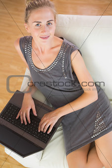 Casual happy blonde relaxing on couch using laptop