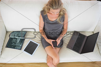 Casual blonde relaxing on couch next to several electronic devices