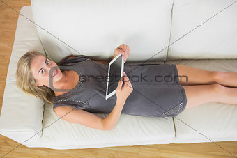 Casual smiling blonde lying on couch using tablet