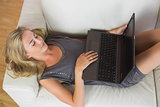 Casual happy blonde lying on couch using laptop
