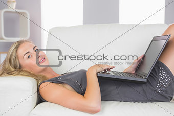 Casual cheerful blonde lying on couch using laptop